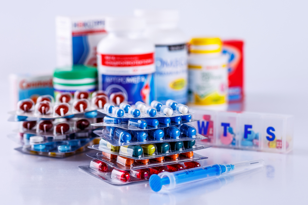 Selection of different types of epilepsy medicines. This includes different colour and shapes of tablets, a dosette box, different bottles of medicines, and a syringe.