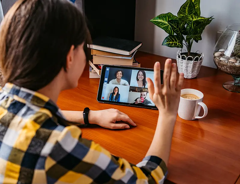 person waving at a tablet device with a video call on screen